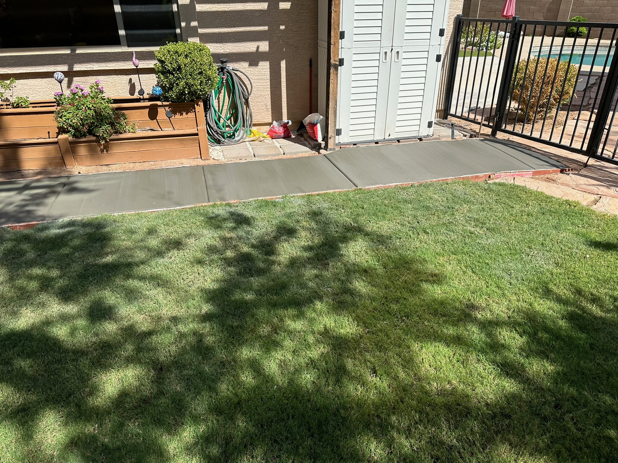 Fresh concrete garden walkway connecting a backyard patio, shed, and pool gate